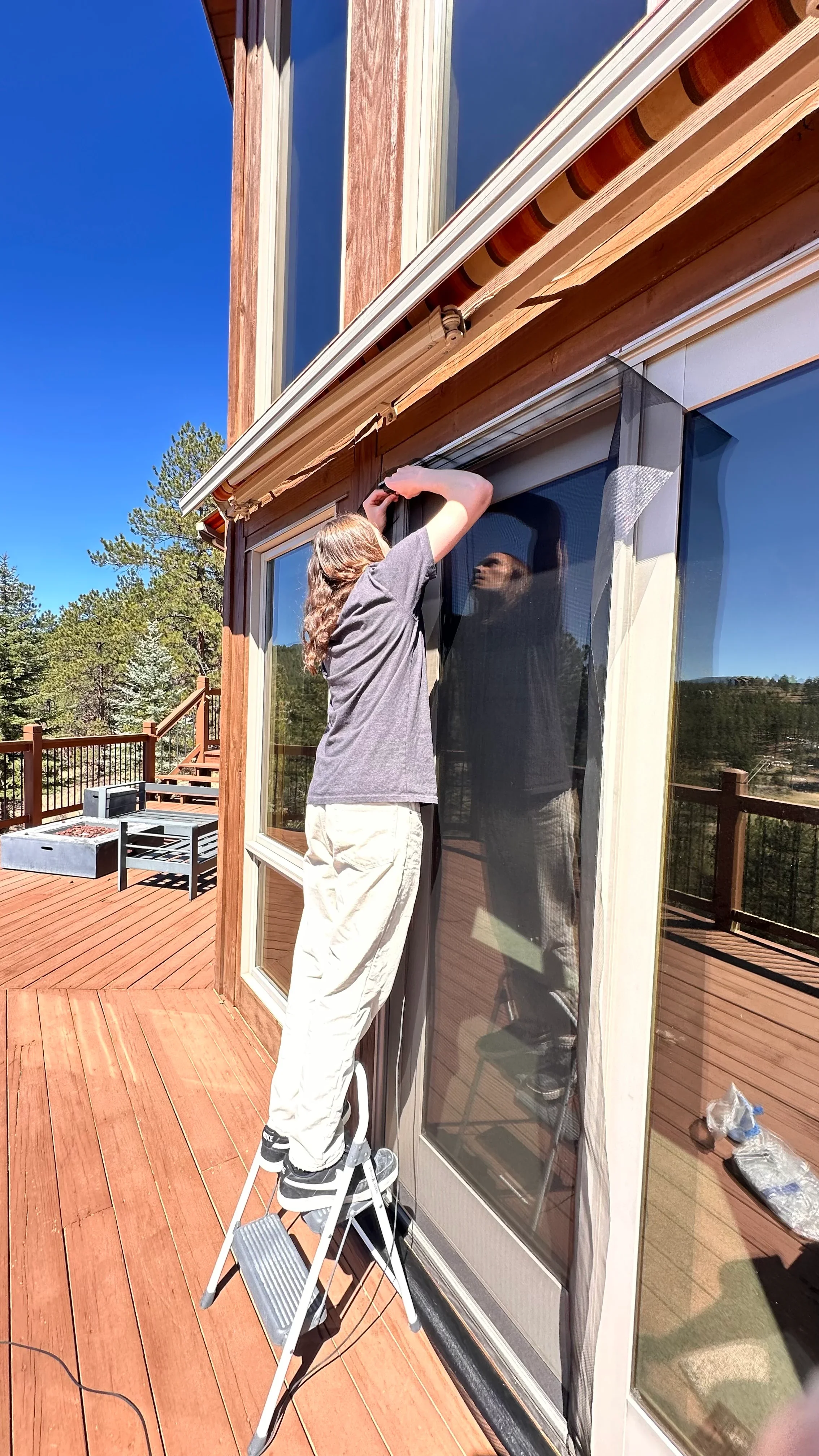Technician installing replacement screen mesh on sliding glass door with mountain forest view