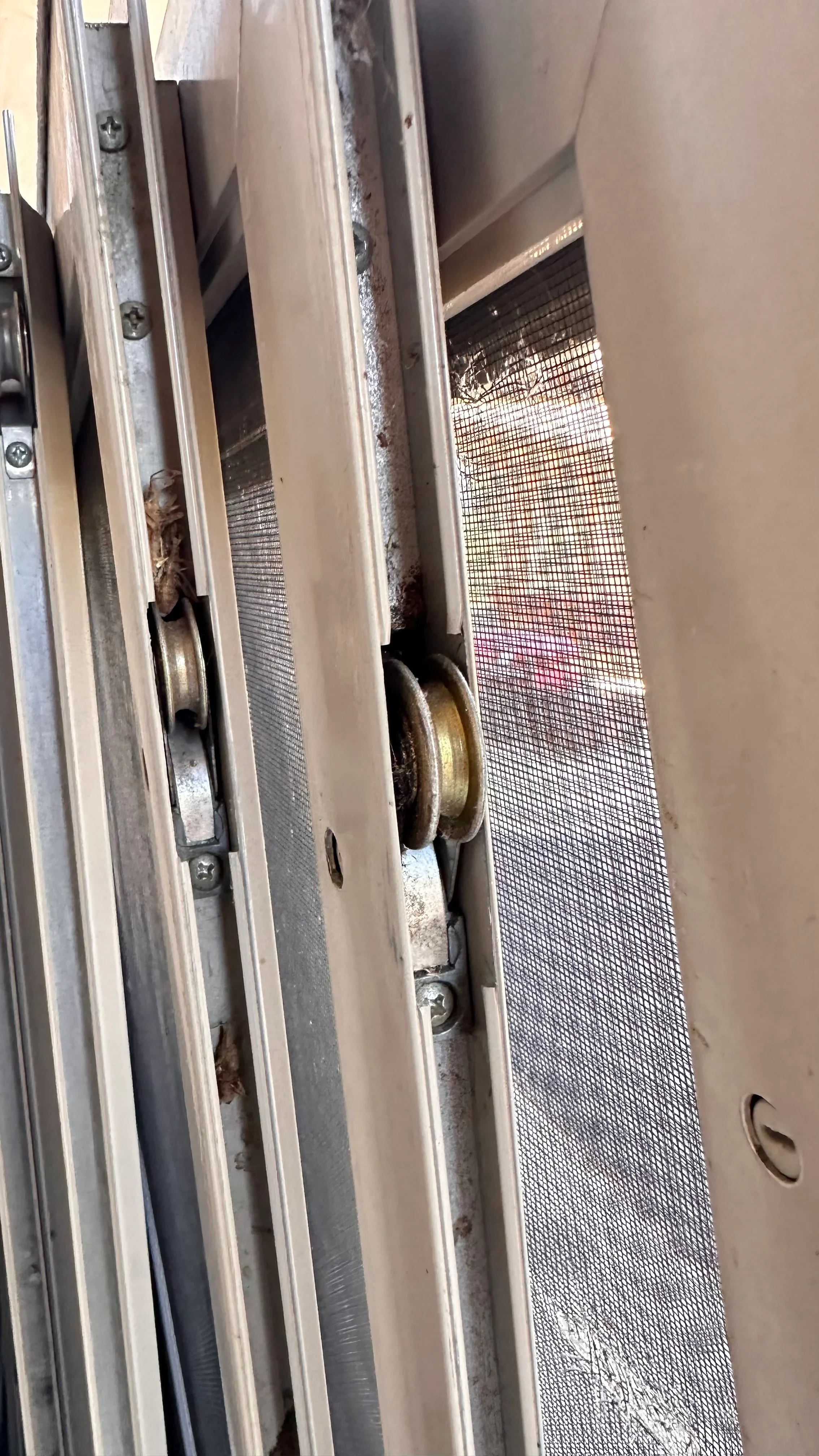 Close-up of sliding glass door track with metal roller and mesh screen visible