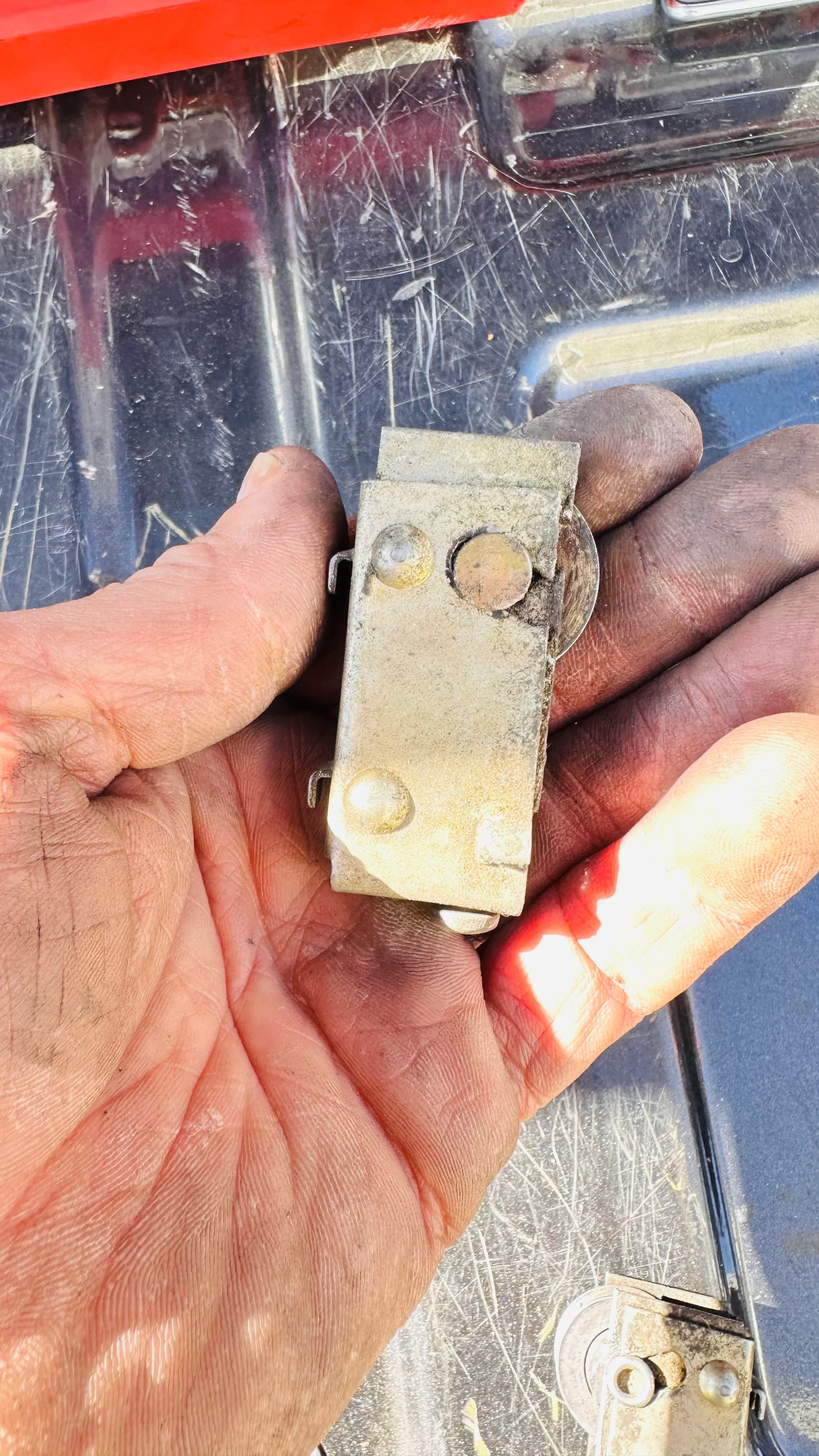 Close-up of corroded brass door hinge with three riveted mounting points held in hand