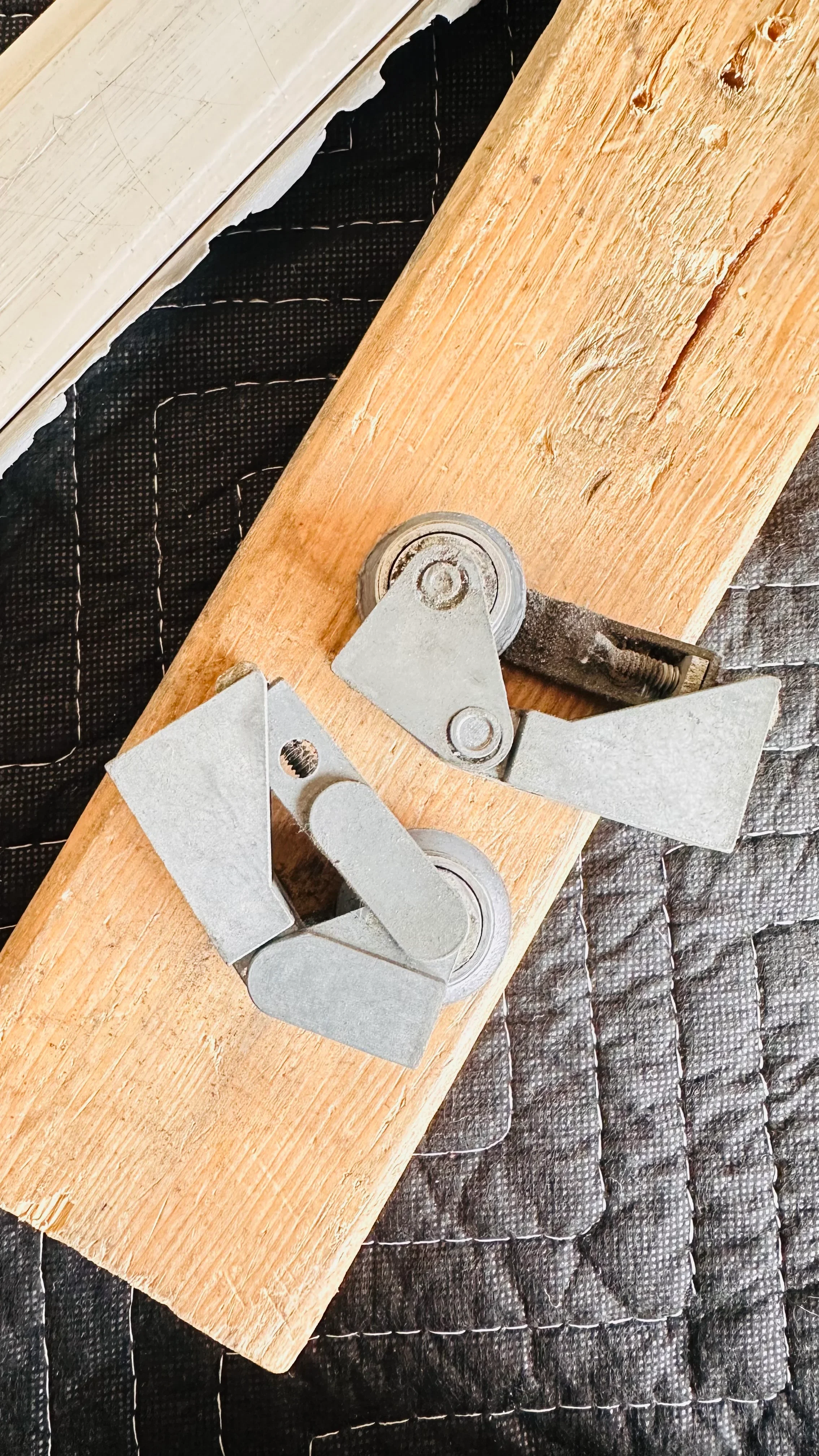 Metal casters and mounting brackets installed on wooden door with black underlayment